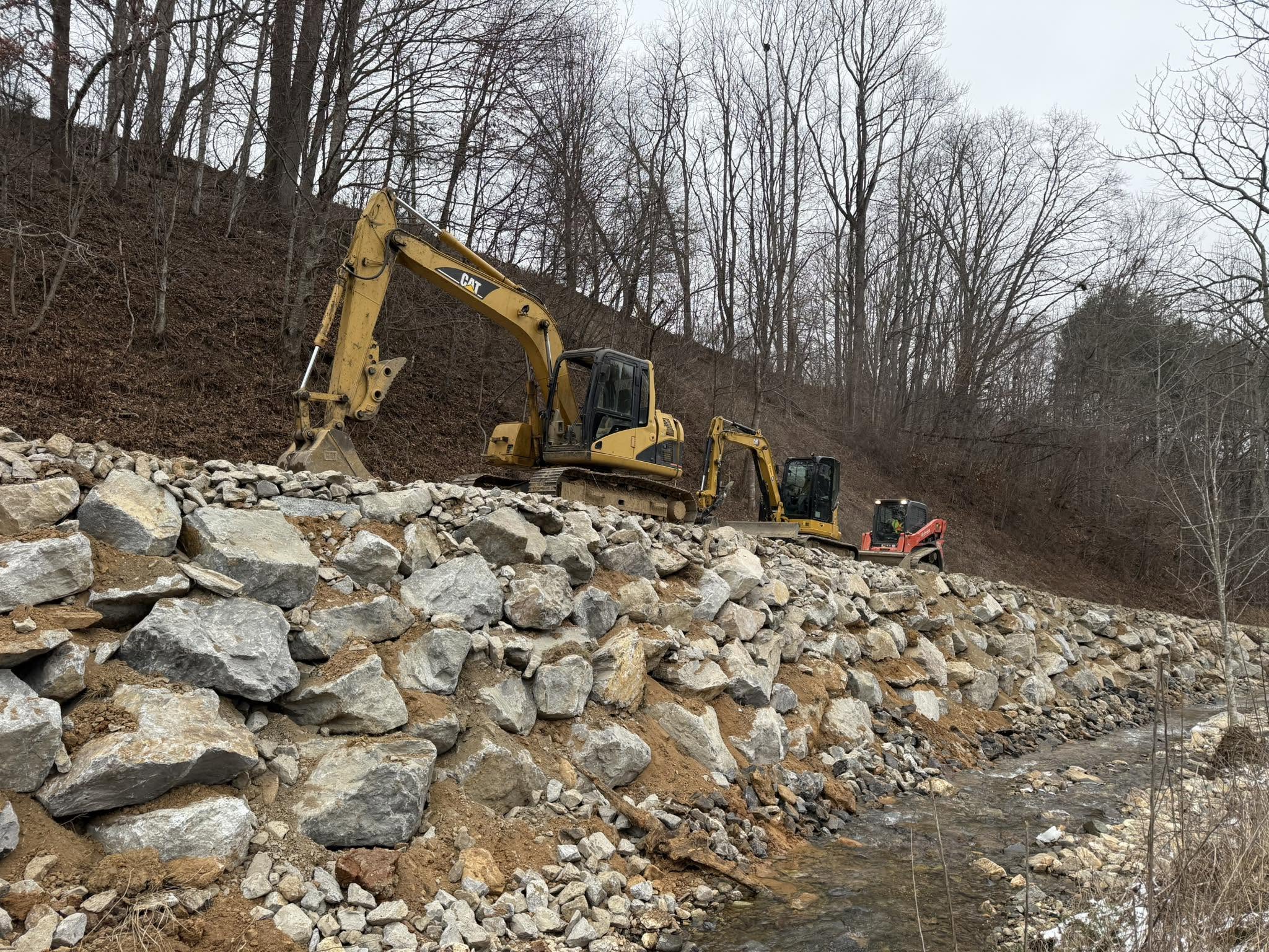 Boulder and riprap retaining wall built along a creek to stabilize the slope, Western NC